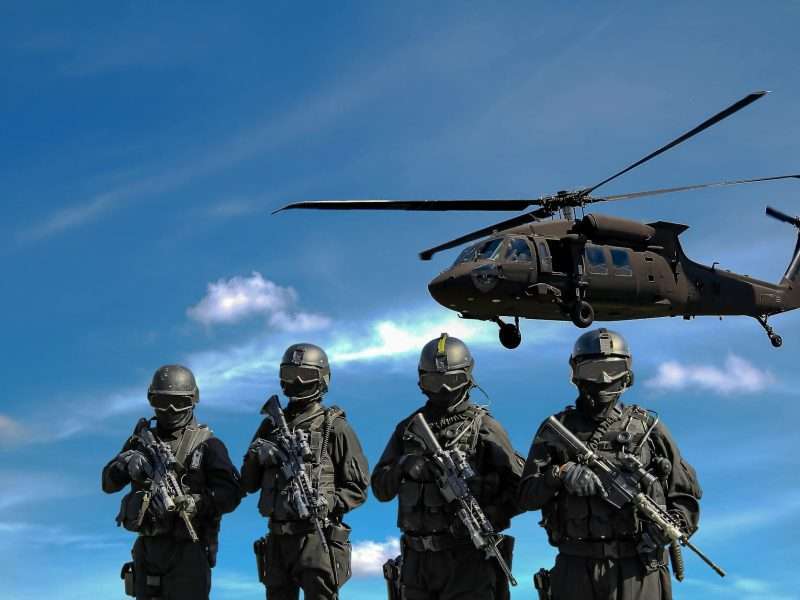 four soldiers carrying rifles near helicopter under blue sky